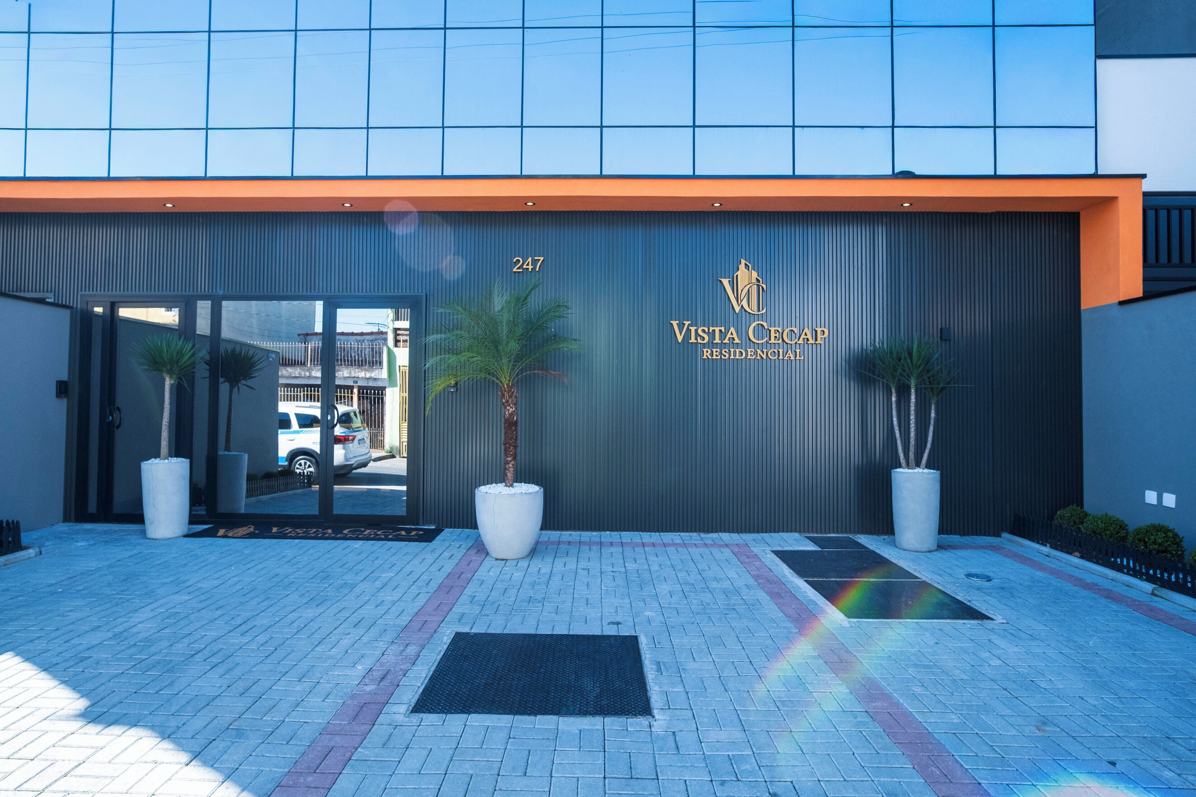 Een moderne gevel met een groot bord voor Vista Ceap Residencial, met het nummer 247, twee potplanten en een verhard entreegebied.