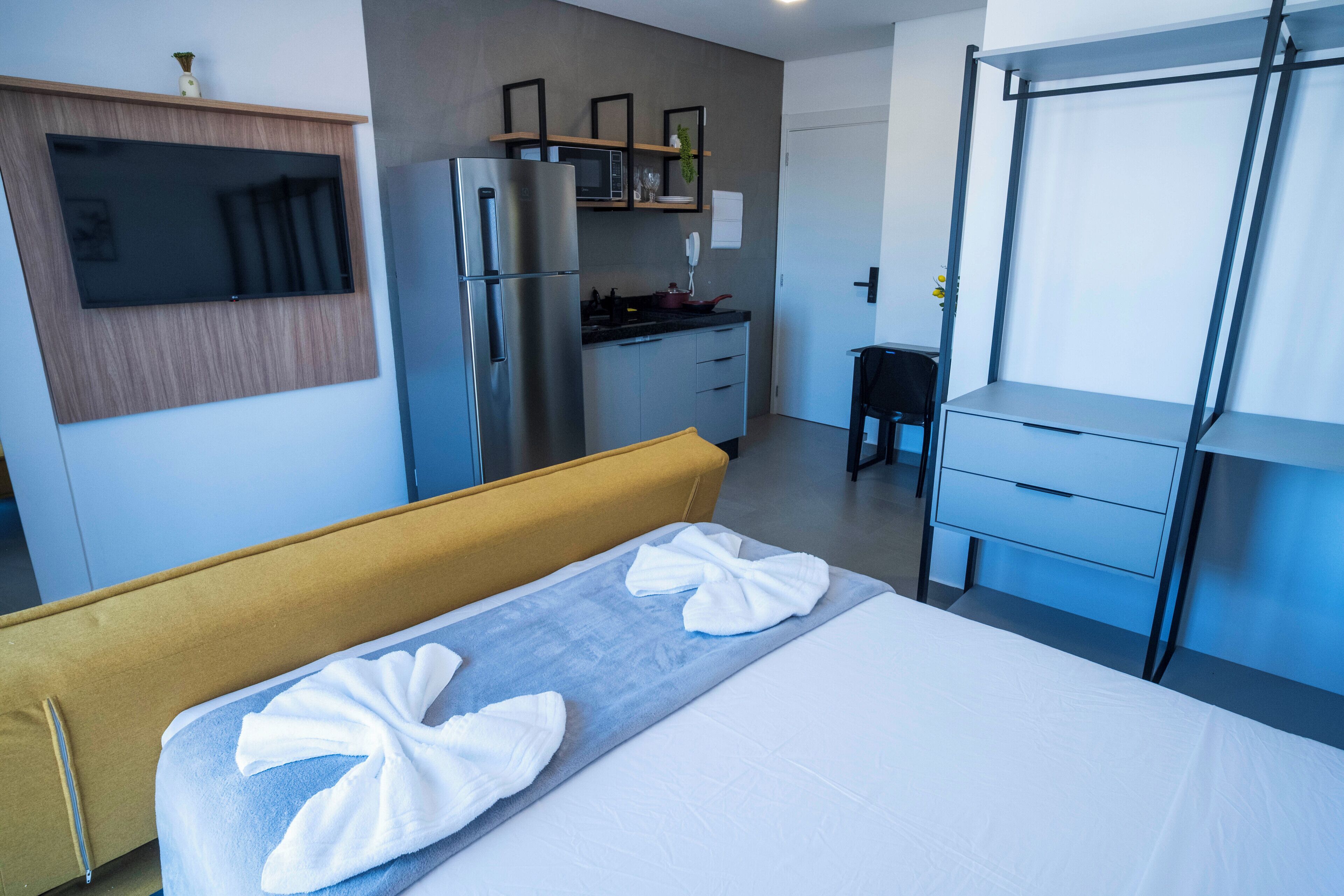 A hotel room with a bed, a sofa, a kitchenette, and a TV.