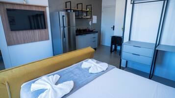 A hotel room with a bed, a sofa, a kitchenette, and a TV.