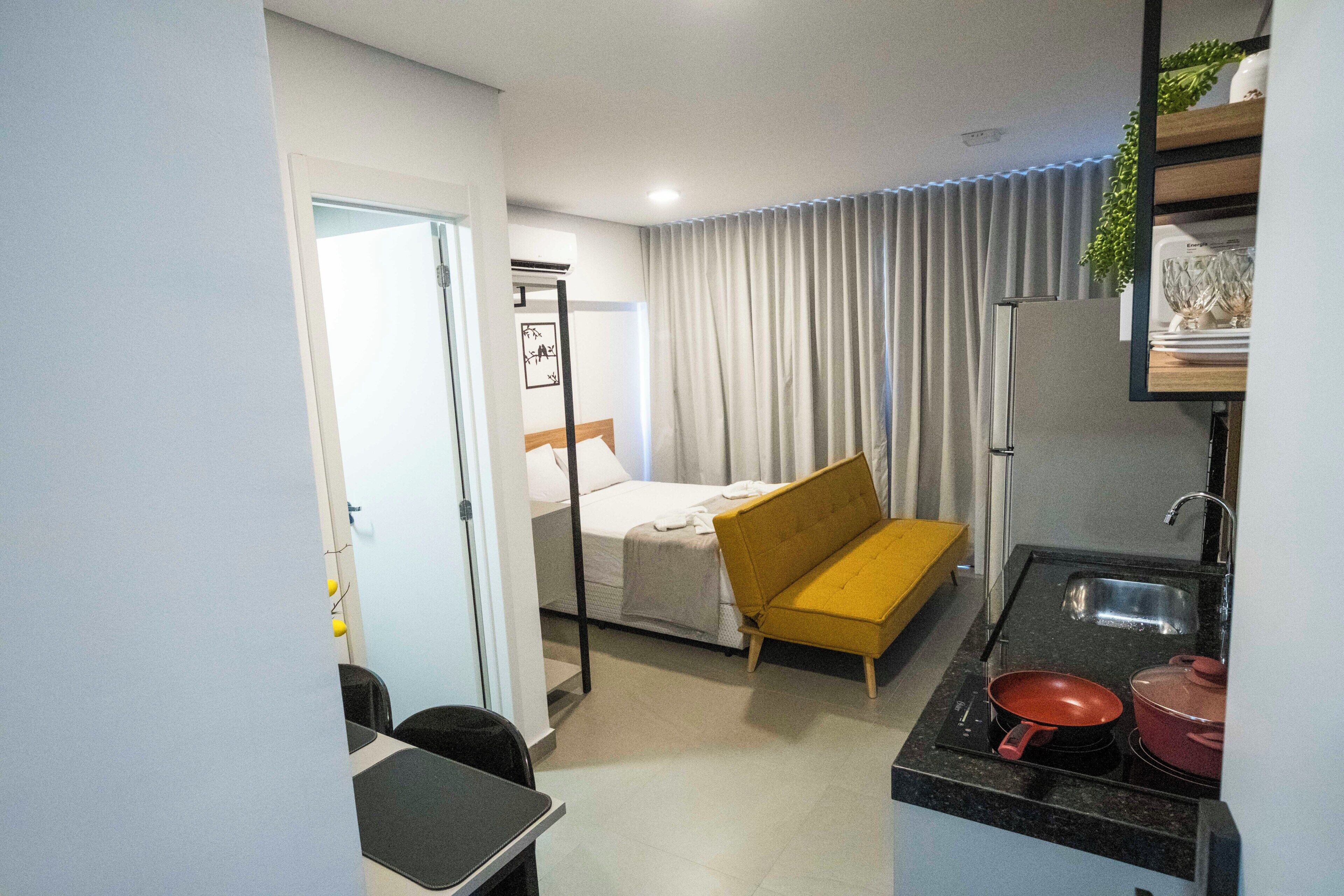 Een compacte hotelkamer met een bed, een slaapbank, een kitchenette en een badkamer.
