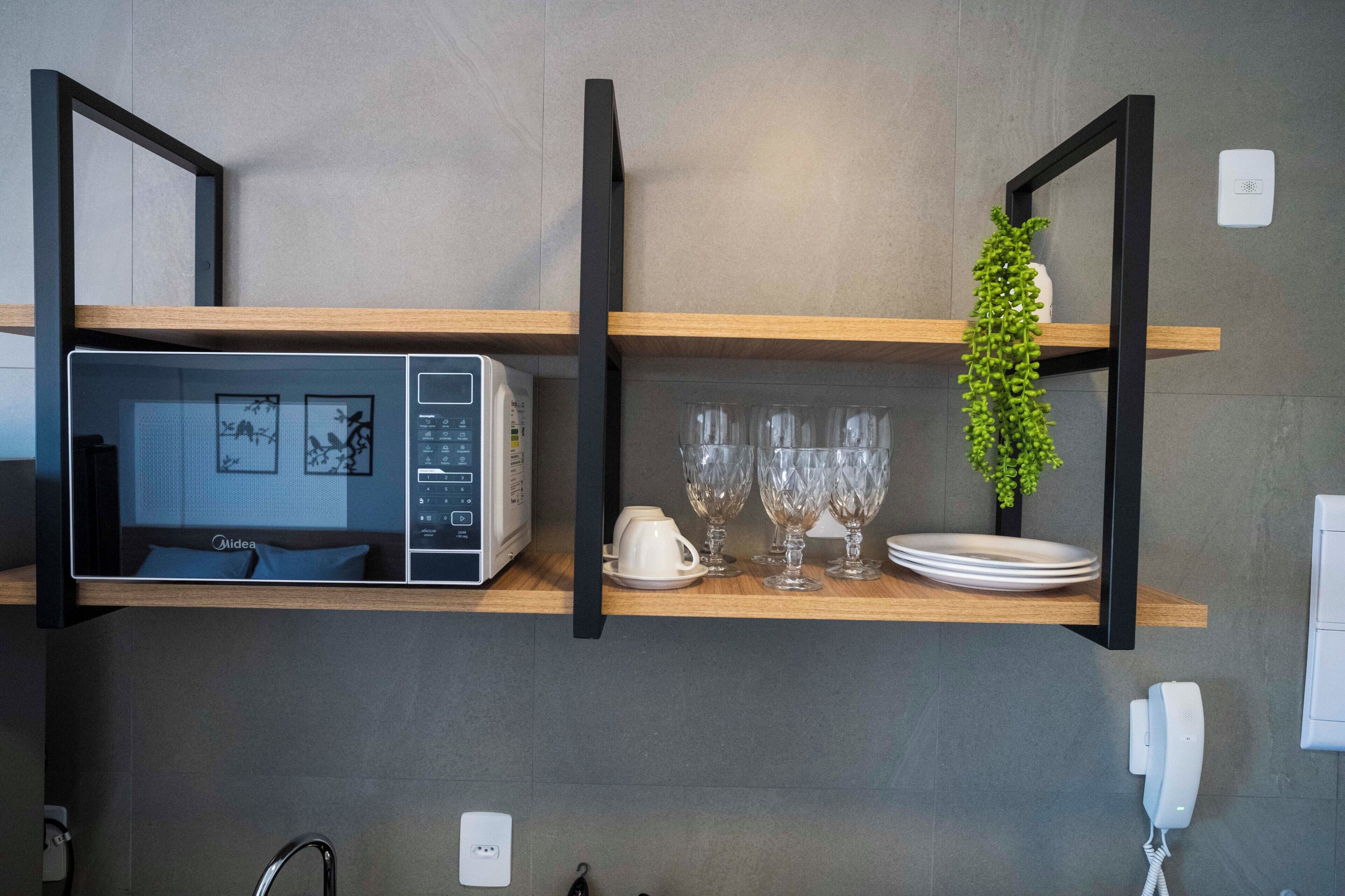 A kitchen with a microwave, glassware, and a plant on a shelf.