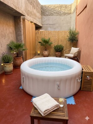 A hot tub in a courtyard with potted plants and a chair.