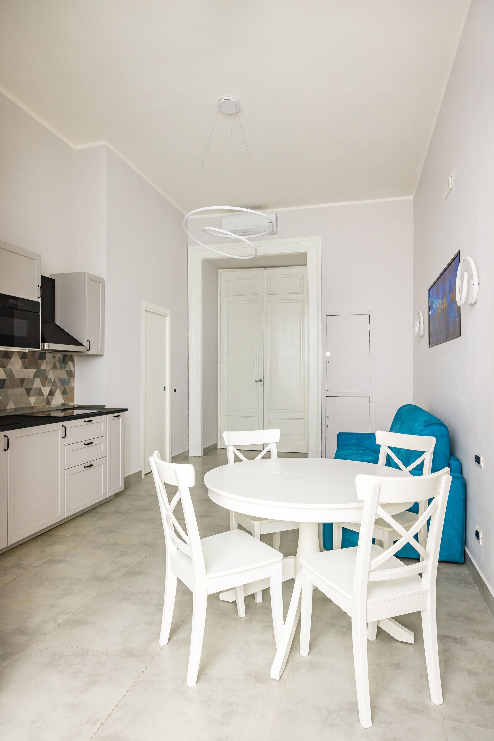 Een moderne keuken met witte kasten, een zwarte oven en een witte eettafel met stoelen.