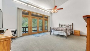 Une chambre à coucher avec un lit, un bureau et une chaise. Il y a une fenêtre qui donne sur des arbres.