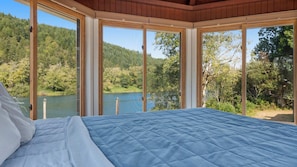 A bedroom with a large bed, wooden ceiling, and a view of a lake surrounded by trees. - Waterview w Dock and Fishing, Wrap around deck (Mapleton)