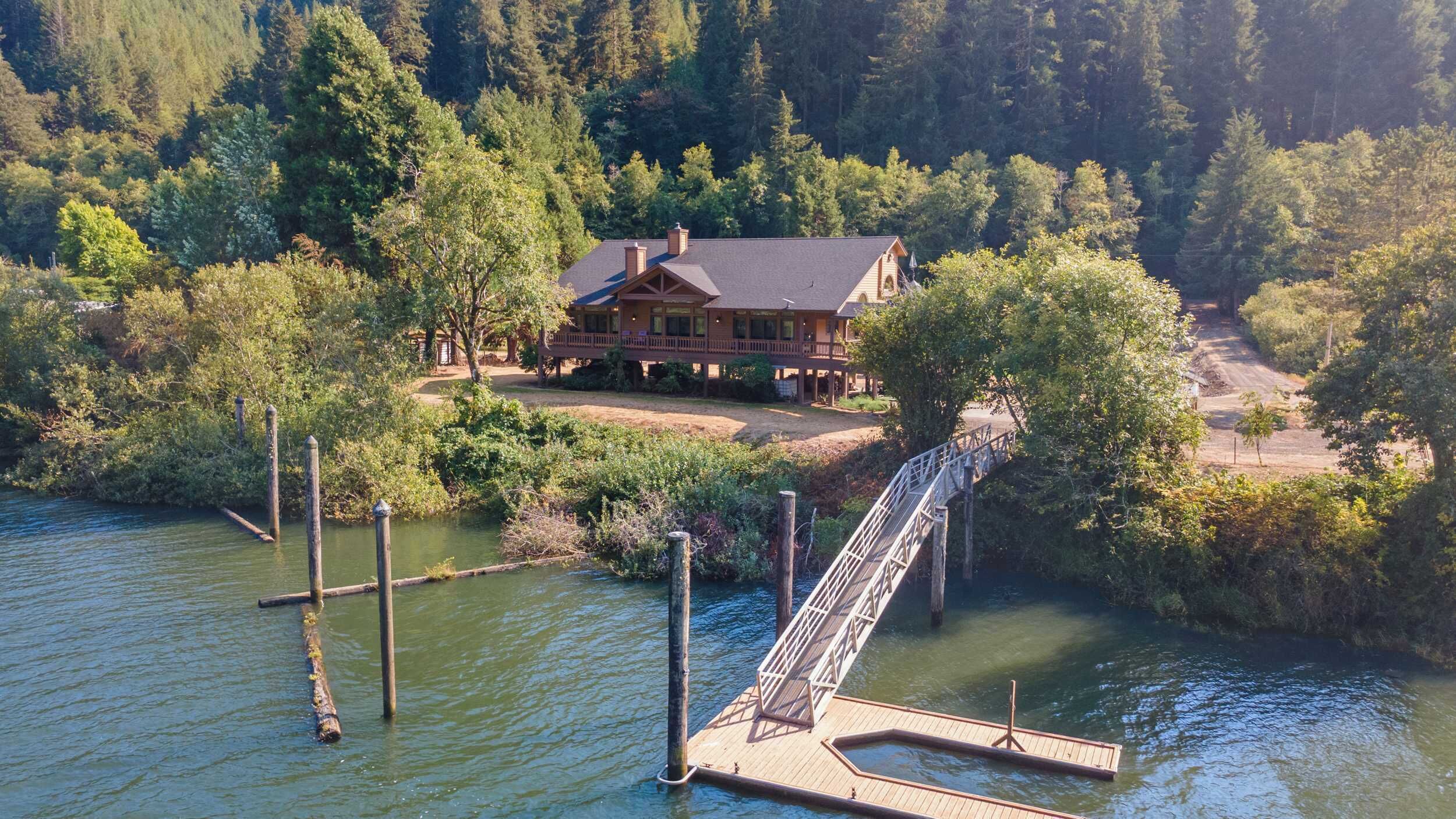 A house with a dock extending into a body of water, surrounded by dense forest.