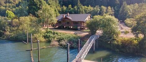 A house with a dock extending into a body of water, surrounded by dense forest.