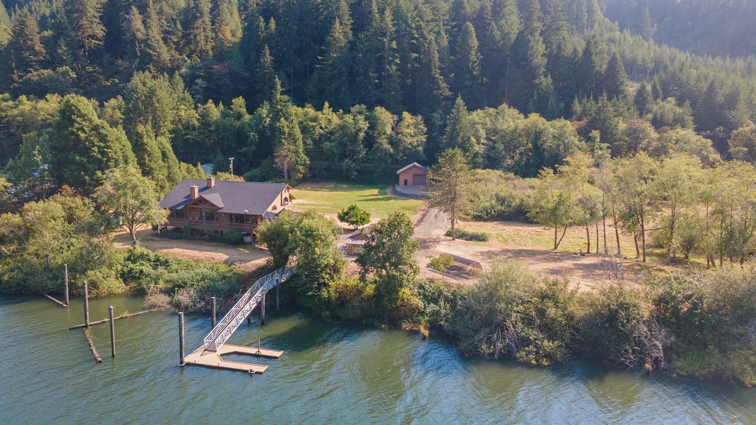 A lakeside property with a dock, a house, and a smaller building, surrounded by dense forest.