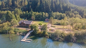A lakeside property with a dock, a house, and a smaller building, surrounded by dense forest. - Waterview w Dock and Fishing, Wrap around deck (Mapleton)