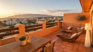 Eine Terrasse mit einem Holztisch, zwei Lounge-Stühlen und einem Topfpflanzen.