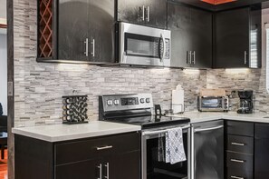 Une cuisine moderne avec des meubles de couleur sombre, un four à micro-ondes en acier inoxydable, une cuisinière à gaz et un four encastré.