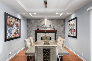 Une salle à manger avec une table rectangulaire, six chaises, un lustre et deux tableaux abstraits accrochés aux murs.