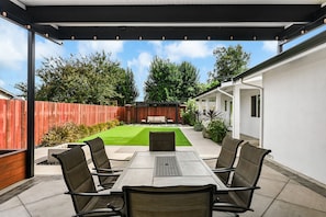 Une terrasse extérieure avec une table et des chaises, une clôture en bois et une pelouse verdoyante.