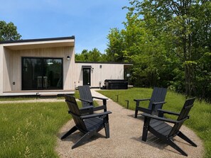 A modern building with a glass door and a patio area with two Adirondack chairs. - Modern Scandi Home on a Private Estate (Harbor Springs)