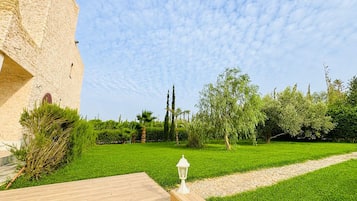 A courtyard with a wooden deck, a white lantern, and a variety of greenery including trees and shrubs.