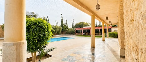 Un espacio al aire libre techado con piscina, piso de baldosas y columnas.