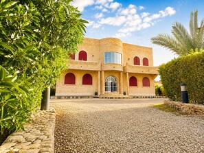 A two-story building with a curved facade, multiple arched windows, and a central entrance with a glass door. - Villa Al Jaouhara - Private Pool, 1-hectare Garden, and Accommodations for 20 Guests (Essaouira)