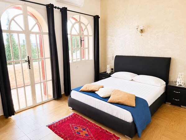 A bedroom with a bed, a nightstand, a lamp, and a window with curtains.