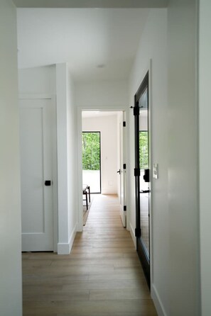 A hallway with a wooden floor, white walls, and a door leading to a balcony with a view of greenery. - Private, modern house with fireplace & hot tub (Harbor Springs)