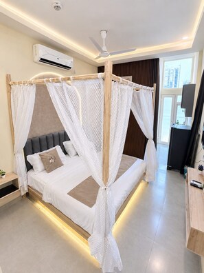 A modern bedroom with a canopy bed, a ceiling fan, and an air conditioning unit. - The Magnolia | Premium Studio By Verve (Greater Noida)