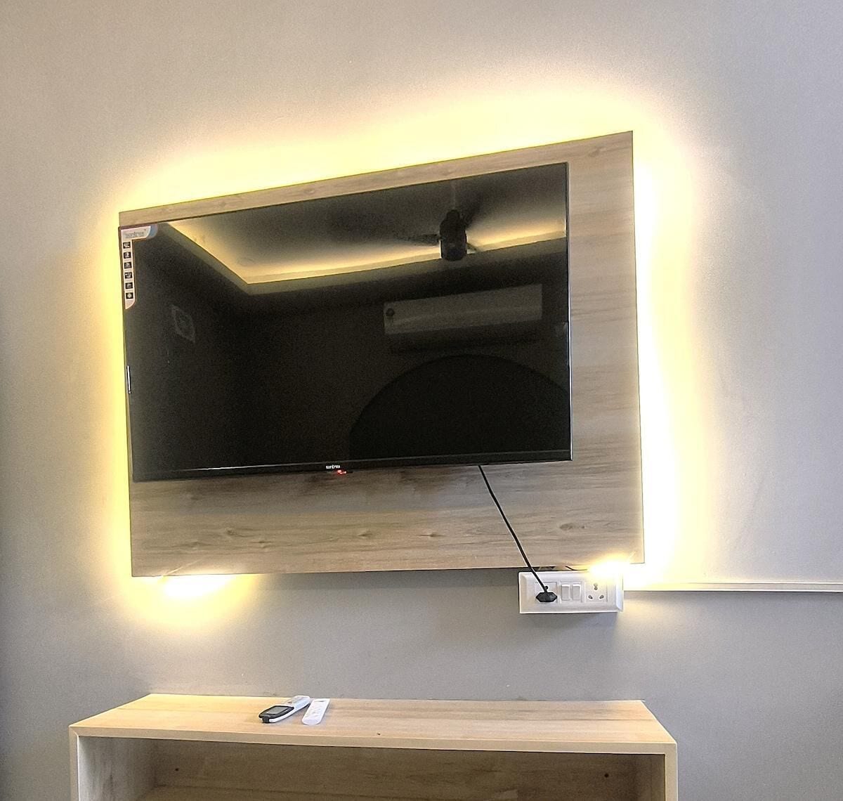 A flat-screen TV mounted on a wall with a wooden shelf below.