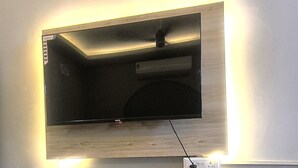 Un televisor de pantalla plana montado en la pared con un estante de madera debajo.