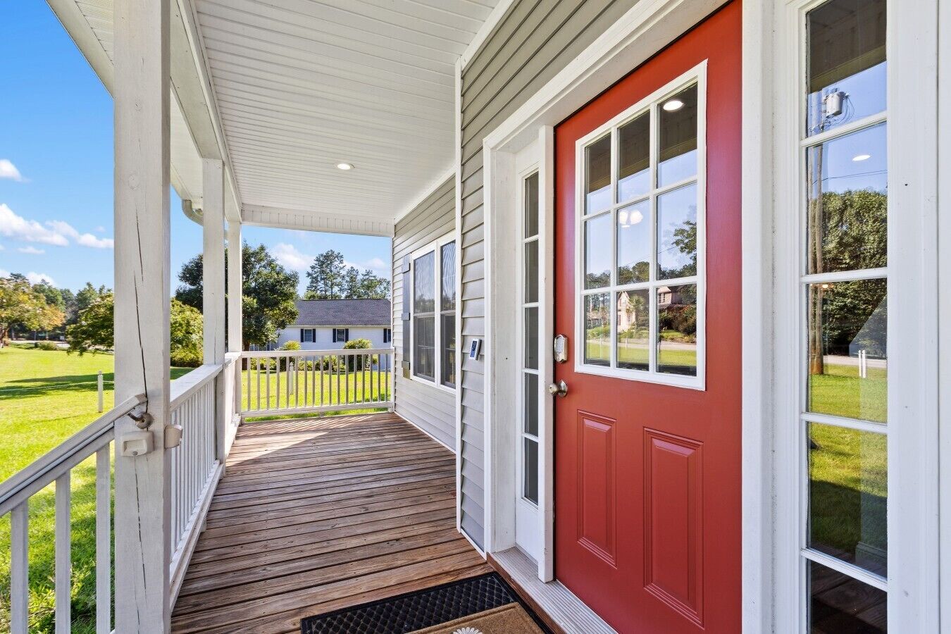 A covered porch with a red door and white trim, leading to a grassy yard.