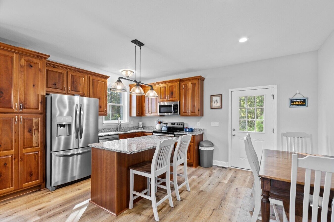 A kitchen with wooden cabinets, stainless steel appliances, a granite countertop, and a dining area with white chairs.