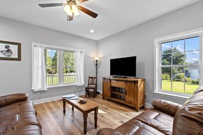 A living room with a wooden entertainment center, leather sofas, a ceiling fan, and large windows with a view of the outdoors.