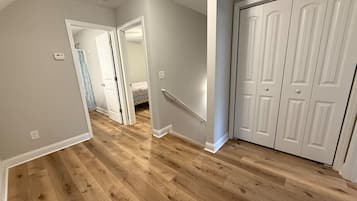 Un pasillo con suelo de madera, paredes blancas y una puerta blanca a la derecha.