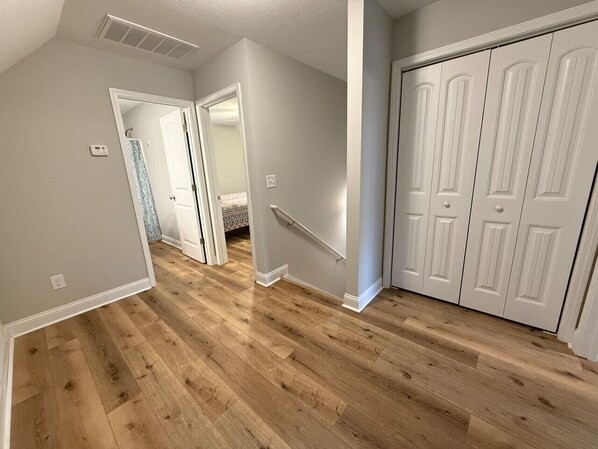 A hallway with wooden flooring, white walls, and a white door on the right.