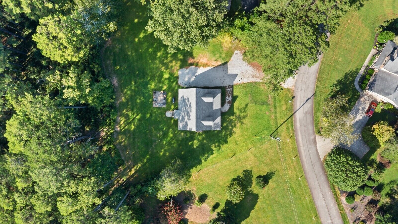 An aerial view of a house surrounded by a well-maintained lawn and dense trees.