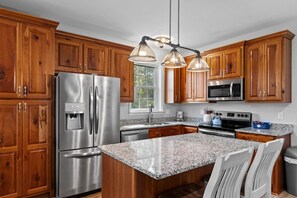 A modern kitchen with wooden cabinets, stainless steel appliances, granite countertops, and pendant lighting.