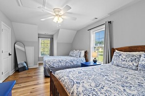A bedroom with two beds, a ceiling fan, a large mirror, and a window with curtains.