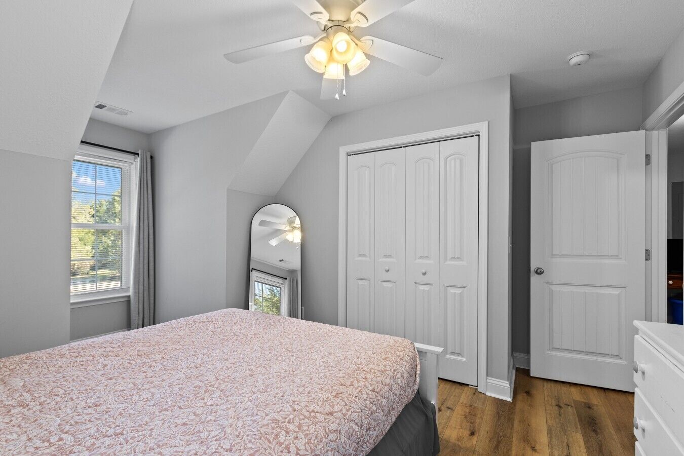 A bedroom with a bed, a ceiling fan, a wardrobe, and a mirror.