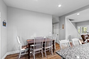 A dining area with a wooden table and white chairs, a kitchen with granite countertops, and a staircase leading to another level. - Walk to Boat Ramp Lake Keowee w/ Parking + Firepit (Seneca)