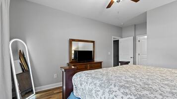 A bedroom with a bed, dresser, mirror, ceiling fan, and a door.