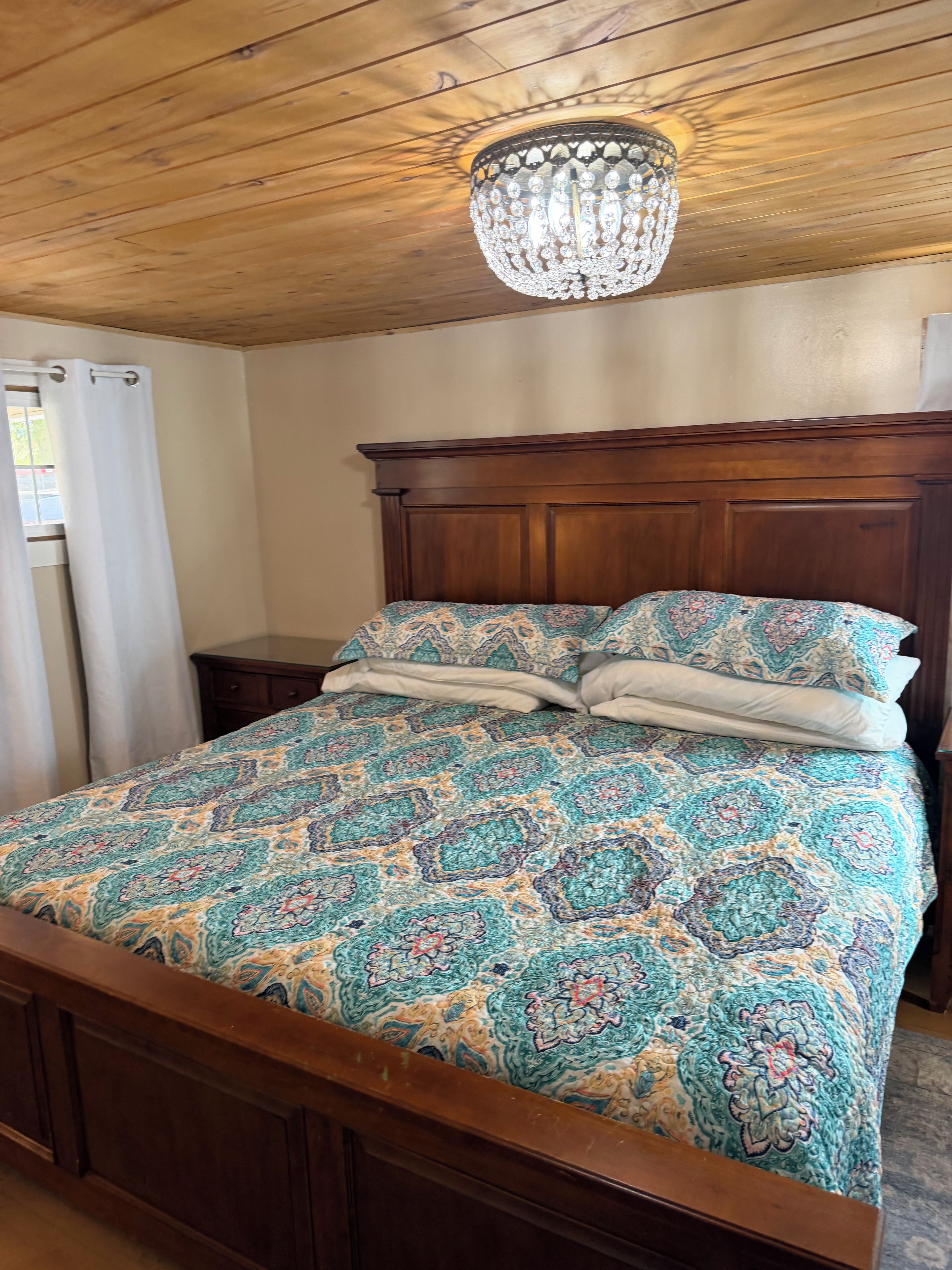 A bedroom with a wooden headboard, a patterned bedspread, and a chandelier.