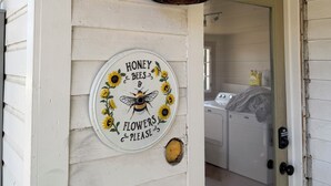 A white exterior wall with a weathered door and a circular sign featuring bees and sunflowers.