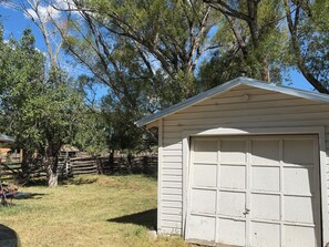 Un petit bâtiment d’un seul étage, doté d’une porte de garage, entouré d’arbres et d’une clôture en bois.
