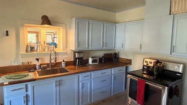 A kitchen with light blue cabinets, a stainless steel oven, and a wooden countertop.