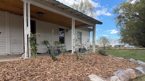 A white house with a porch, a covered area, and a garden with mulch and rocks.