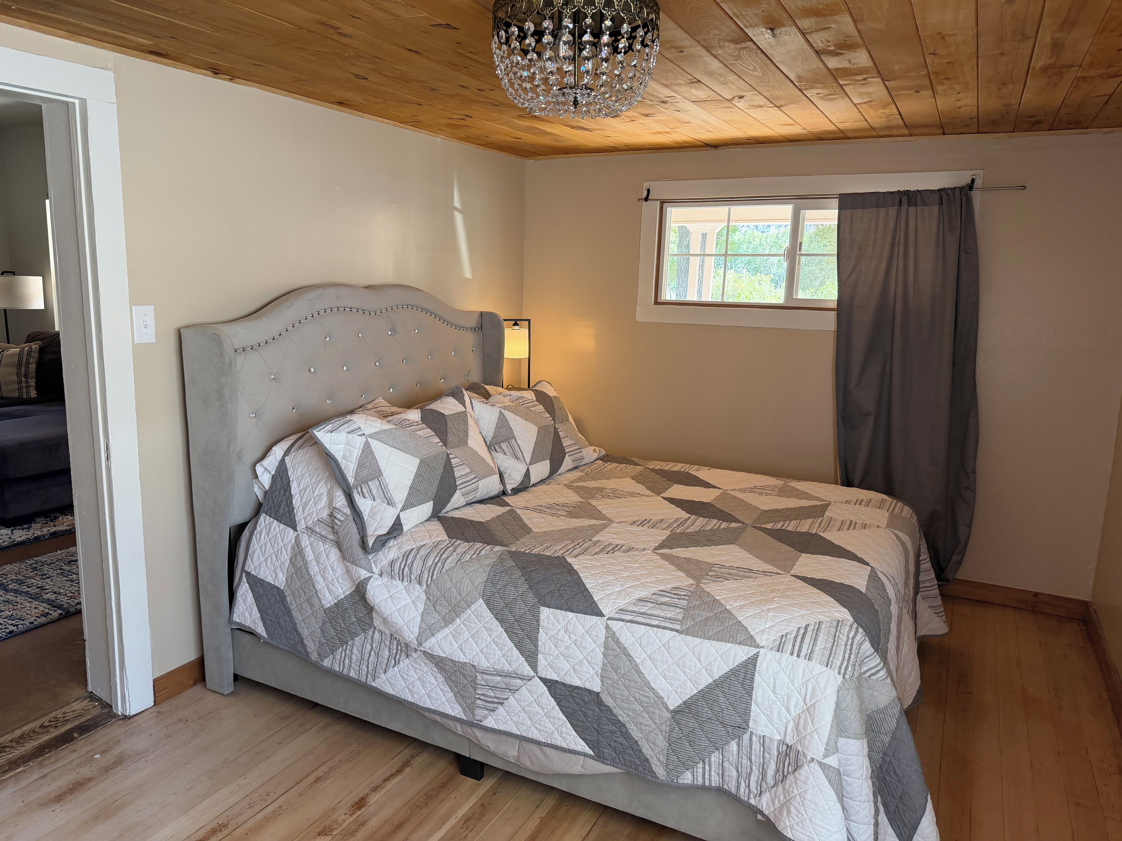 Une chambre à coucher avec un lit, une fenêtre avec des rideaux, un lustre et un plafond en bois.