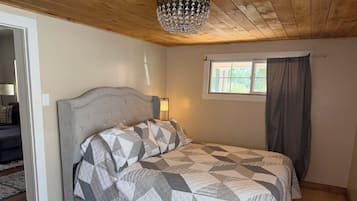 Une chambre à coucher avec un lit, une fenêtre avec des rideaux, un lustre et un plafond en bois.