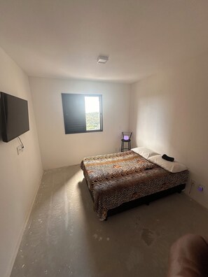 Un dormitorio con cama, televisión, ventana y una silla.