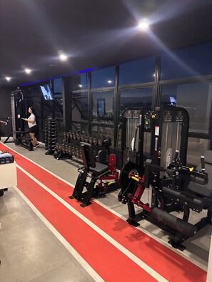 A gym with various exercise equipment, a red running track, and a city view through large windows. - Luxury Apartment in Alphaville Barueri (Barueri)