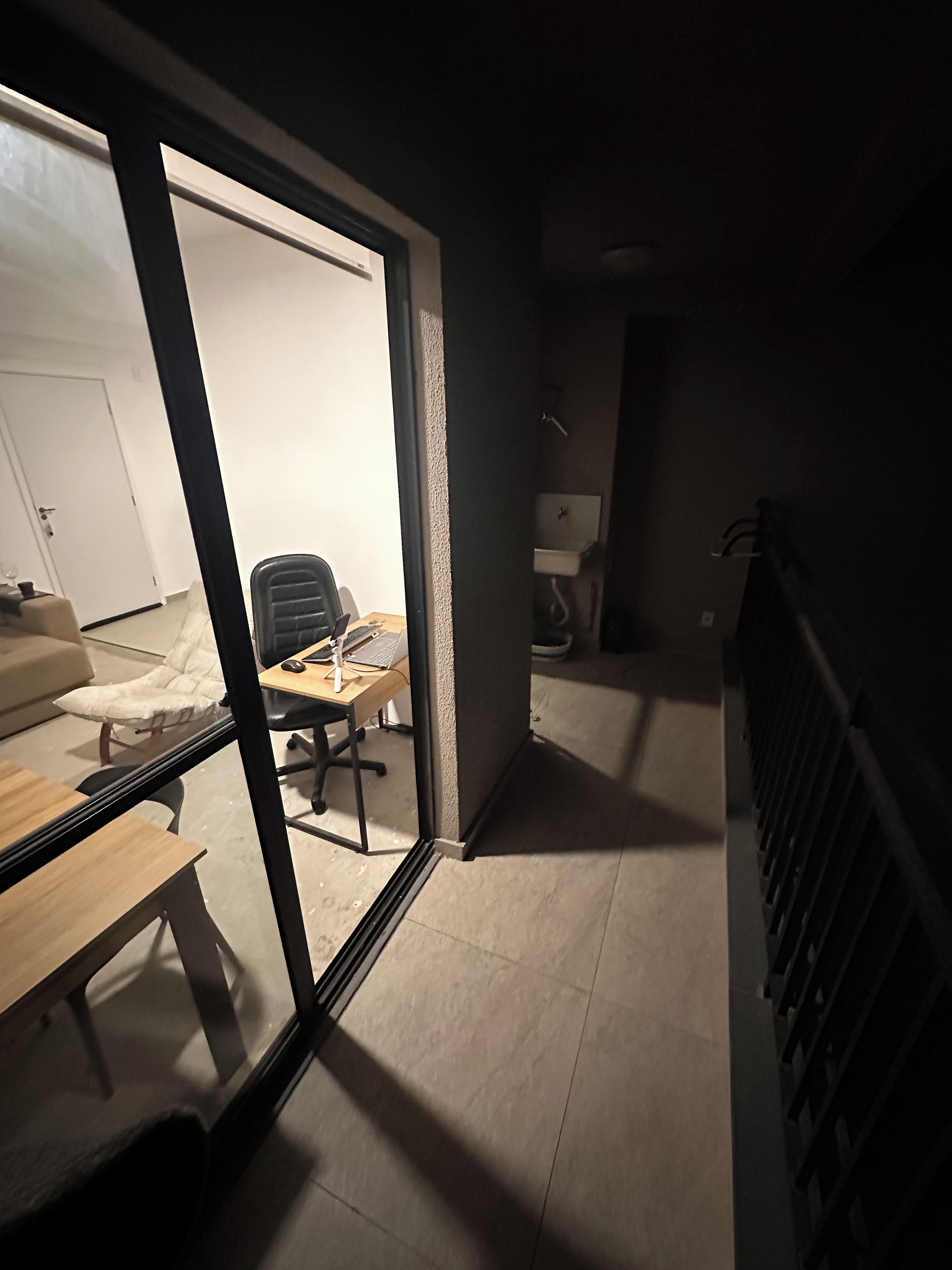 A room with a large sliding glass door leading to a living area, a desk with a computer, and a chair.