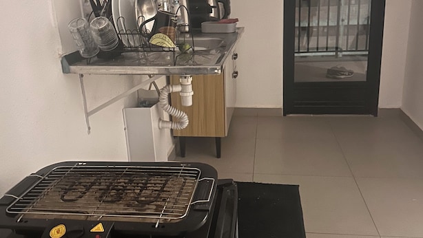 Uma cozinha compacta com churrasqueira, pia e fogão. Há uma janela com vista para um edifício.