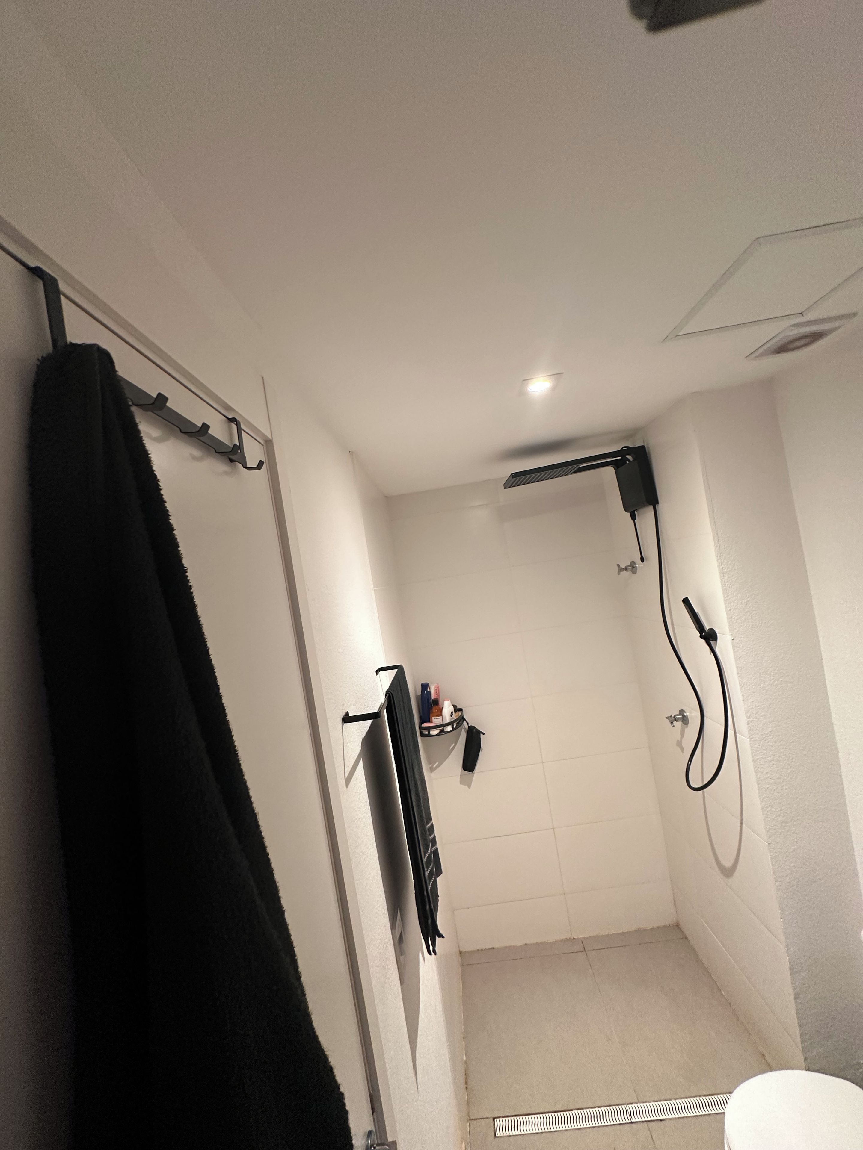 A bathroom with a shower, a towel rack, and a small shelf with toiletries.
