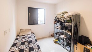 Um quarto pequeno com cama, guarda-roupa e janela.